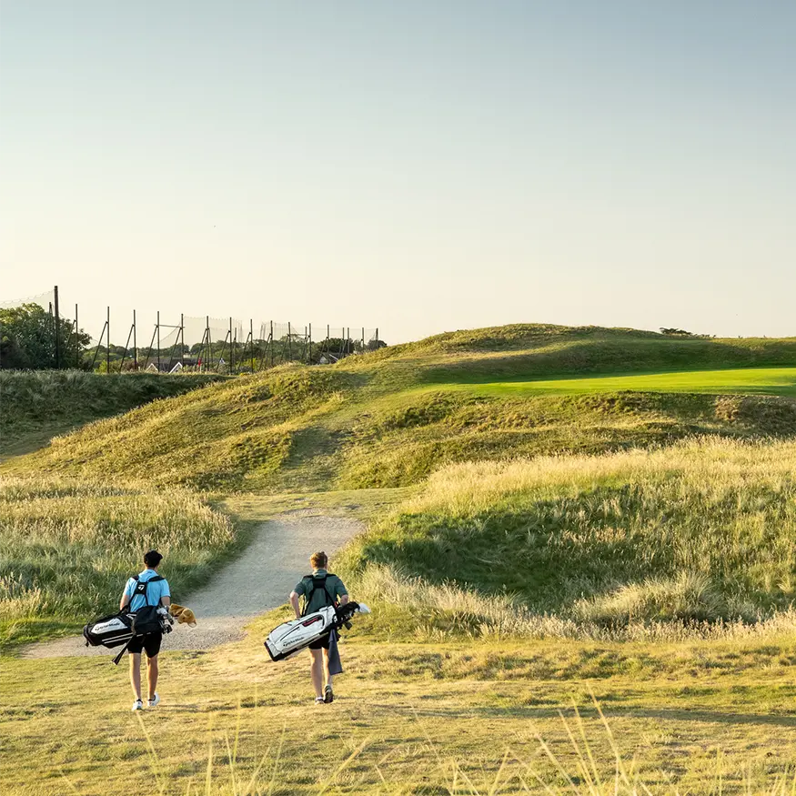 Men with golf bags walk across green